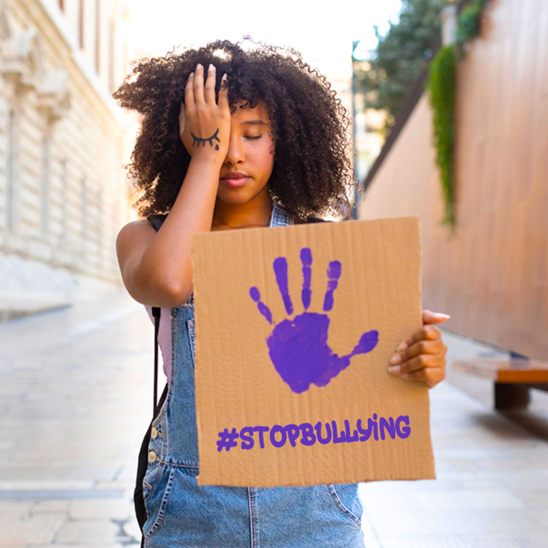 Niña tapándose un ojo con un cartel en mano que dice STOP BULLYING.