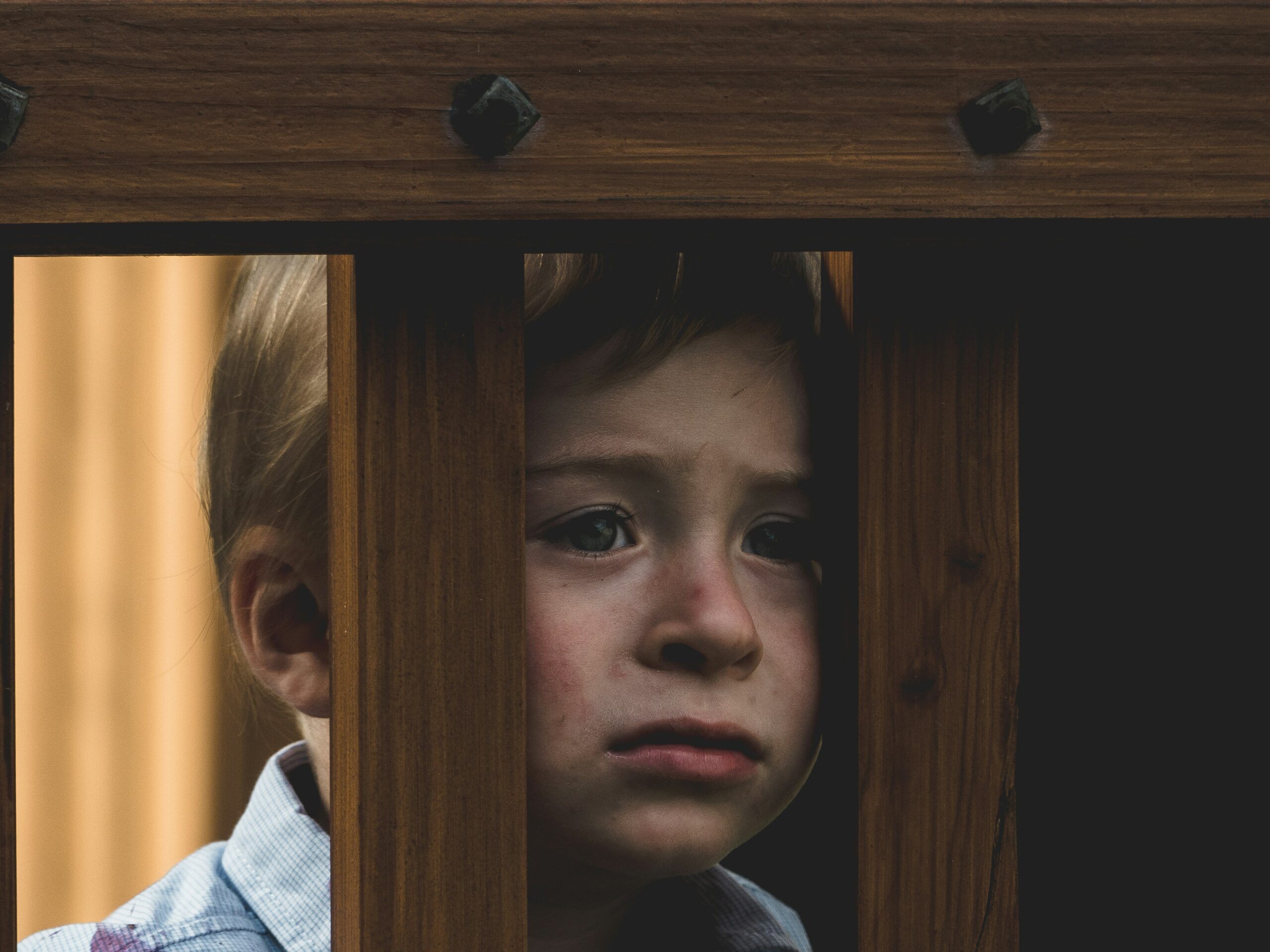Niño triste mirando detrás de unas rejas de madera